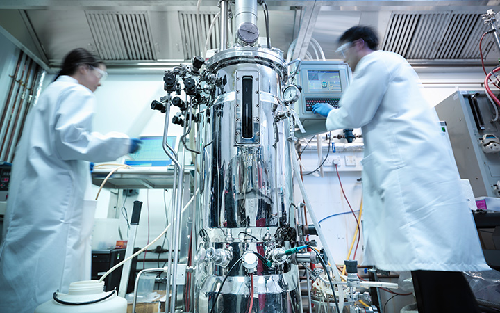 Scientists next to a bioreactor working on protein production in a laboratory