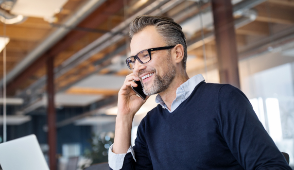 We will be delighted to answer any questions you may have Man in glasses in business office on phone while working on laptop