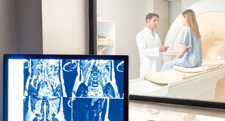 SCHOTT radiation shielding glazing provides protection from harmful radiation Male doctor talking to female patient sitting on MRI equipment in front of a display